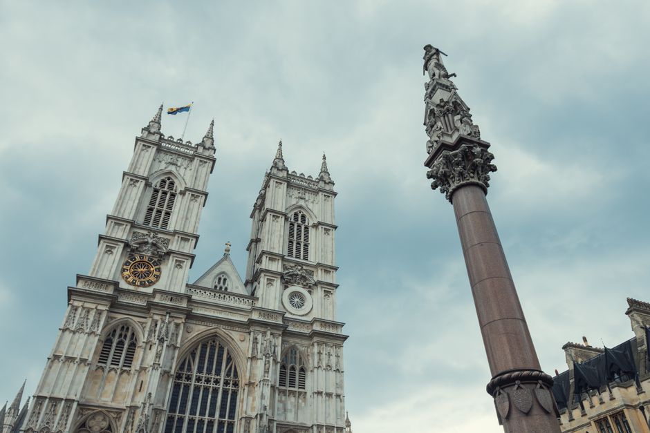 Interior view of a historic church or cathedral within Westminster Abbey, featuring high vaulted ceilings, intricate stone columns, stained glass windows, and a central altar on a raised platform. The