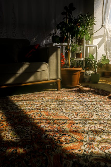 A close-up view of a living room corner featuring a traditional patterned rug with shades of orange, cream, and navy, spread out on a wooden floor. Part of a light-colored upholstered sofa with wooden